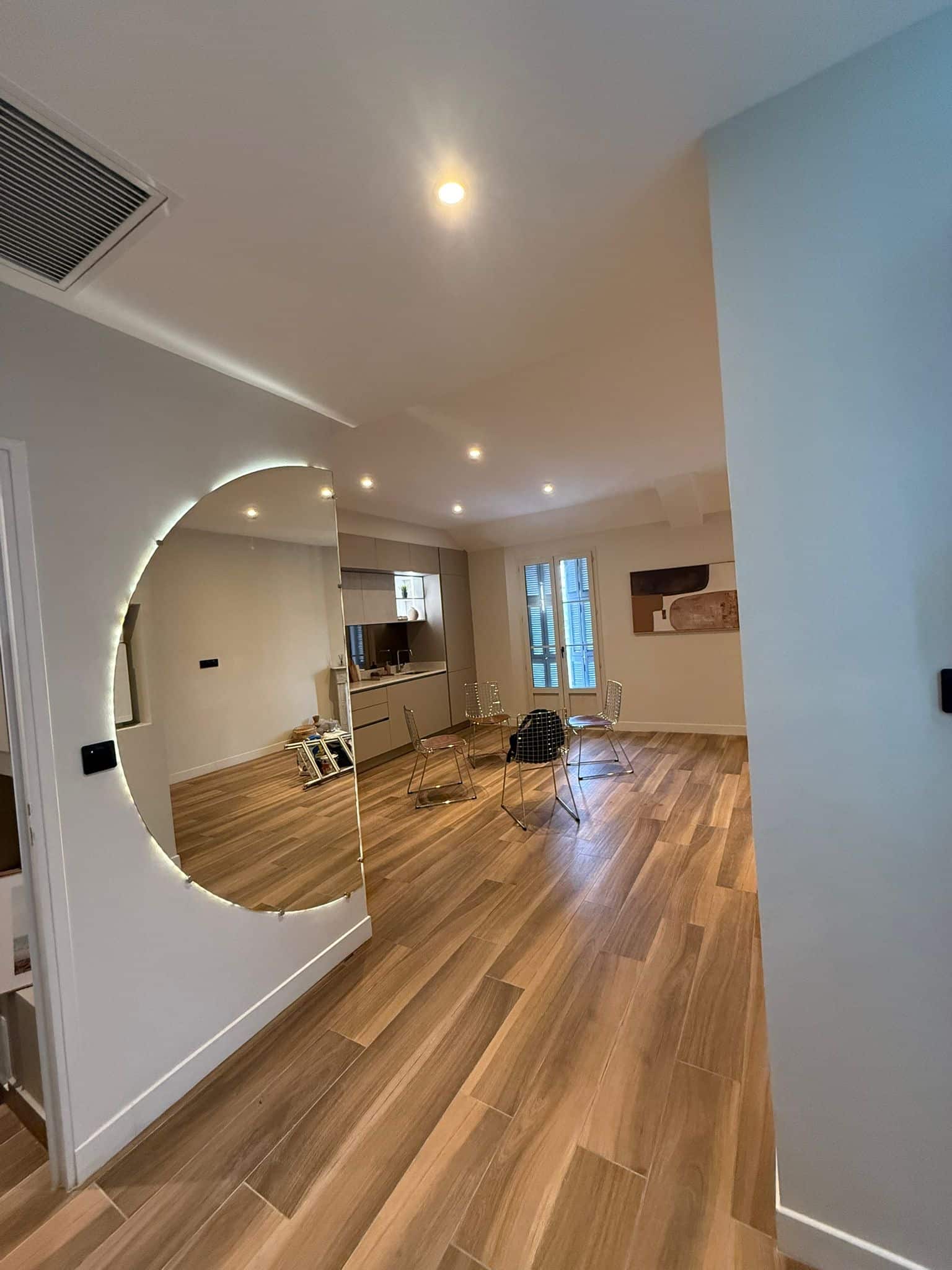 Miroir Design Rétroéclairé pour un Salon Moderne et Chic Grand miroir rond rétroéclairé dans un salon moderne avec parquet en bois et mobilier design.